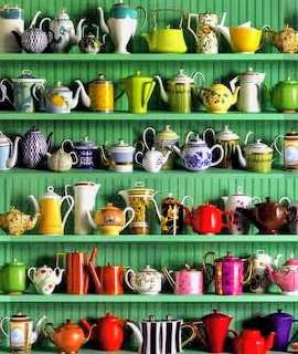Dozens of colorful teapots of various shapes and patterns displayed on bright green shelves