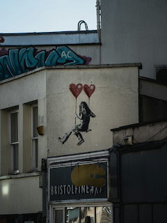 Street art mural of a girl with two red heart balloons painted on a building wall