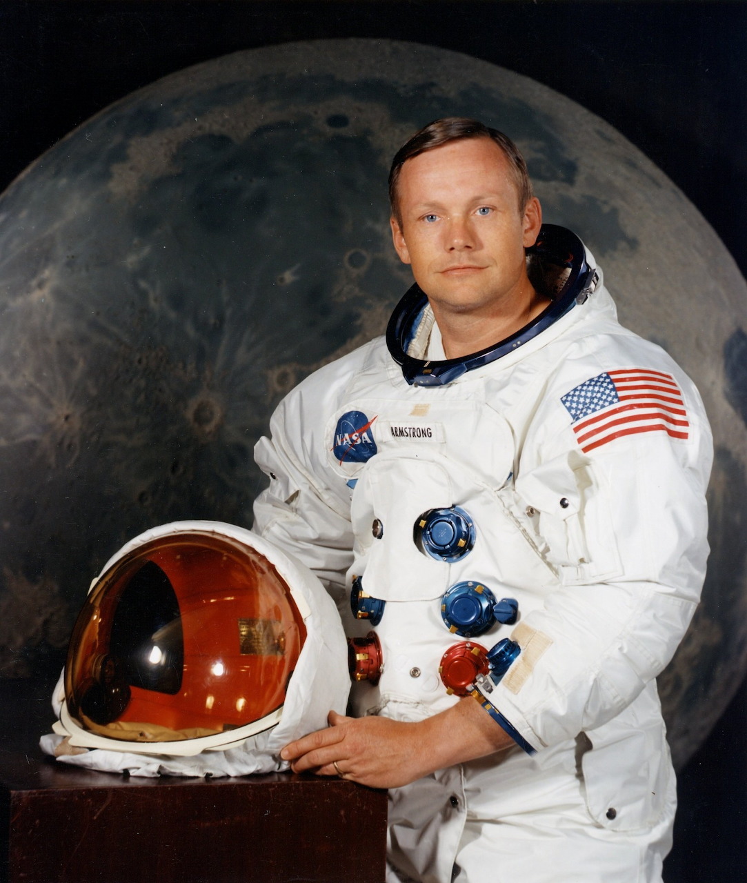 Astronaut Neil Armstrong in white NASA suit holding red and white helmet with Earth behind him