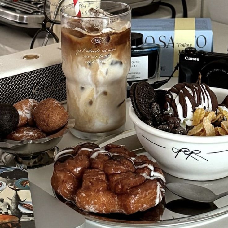 Iced coffee with milk swirls next to assorted chocolate pastries and donuts on plates
