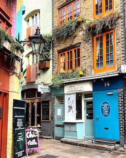 Colorful narrow alley with brick buildings, orange window frames, blue shopfront, and a vintage lamp