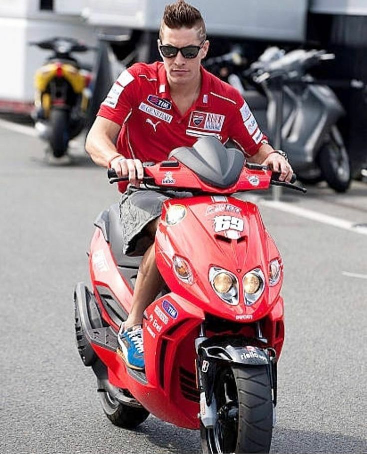 Man wearing sunglasses riding a red scooter on a street