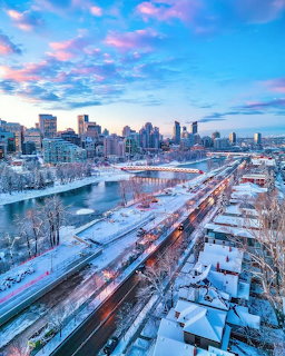 Snow-covered Calgary cityscape at sunset with pink and blue sky, river, and downtown skyline