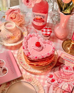 Pink layered cake with cherries, roses, glassware and vintage crockery on checkered tablecloth