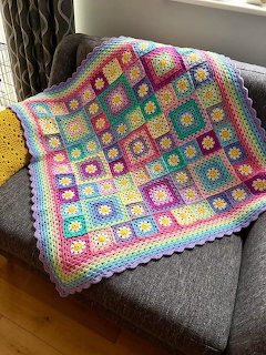 Colorful crocheted granny square blanket draped over a gray armchair