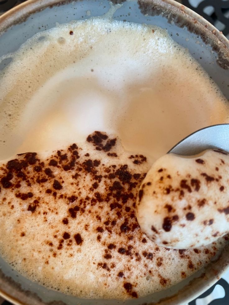 Cappuccino with foam and cocoa powder in ceramic cup, spoon on edge