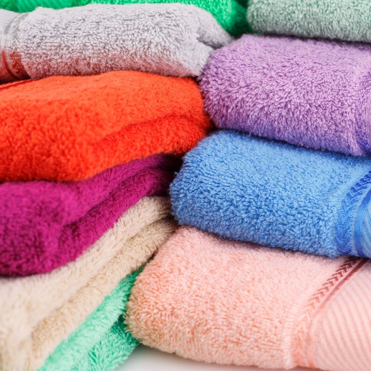 Close-up of stacked colorful bath towels in pink, purple, blue, green, orange, and cream
