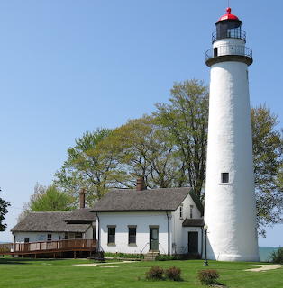 White cylindrical lighthouse with red lantern room beside white keeper's house on green lawn