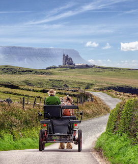 Horse carriage on rural road approaching castle on green hillside under blue sky