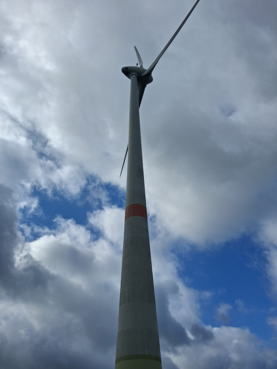 Low-angle view of a wind turbine rising into a cloudy blue sky