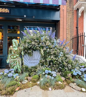 Lavish floral arrangement with greenery and blue flowers outside a London storefront