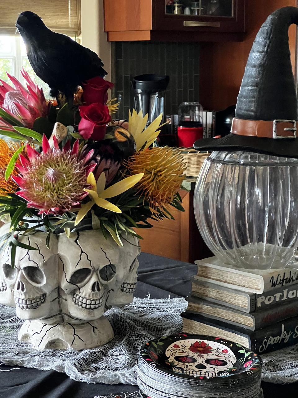Vibrant fall flowers in skull-shaped vases with black witch hat decorations on kitchen counter