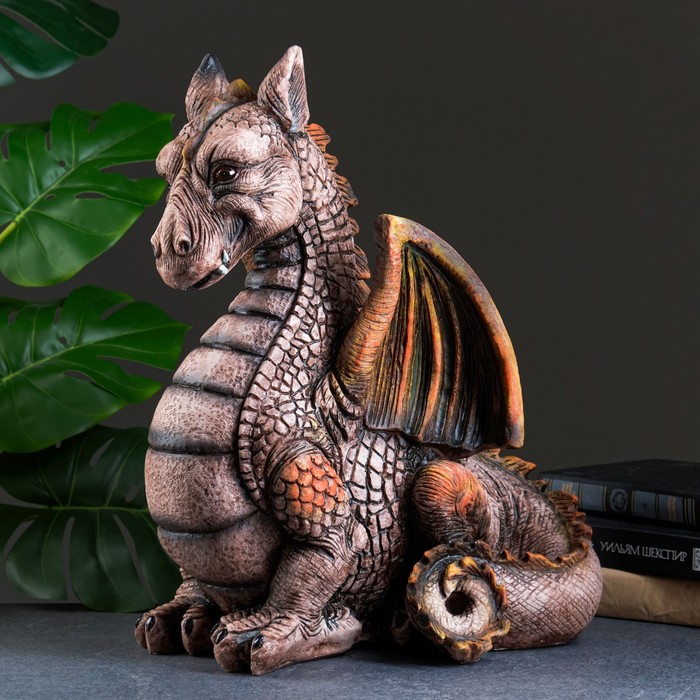 Decorative dragon figurine with textured scales and orange wings next to green leaves