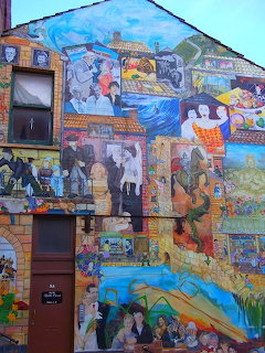 Colorful street art mural covering the side of a building with many painted scenes and figures