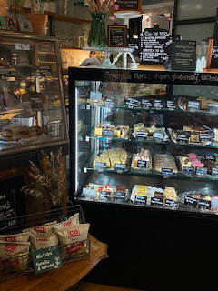 Glass display case in a café filled with sandwiches and snacks, chalkboard menu above