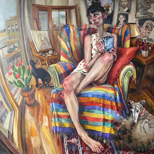 Woman in pink dress sitting on rainbow striped chair in decorated room with cat and artwork