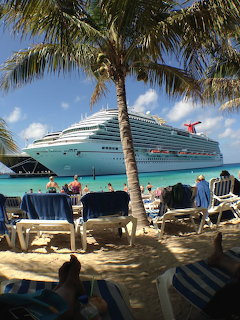 Large cruise ship seen from a tropical beach with palm trees and lounge chairs on the sand