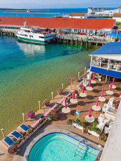 Aerial view of Mackinac Island waterfront with ferry boats, harbor, patio with pink umbrellas, and pool
