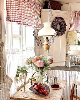 Cozy country kitchen with gingham curtains, vintage lamp, fresh flowers, and red apples on a wooden table