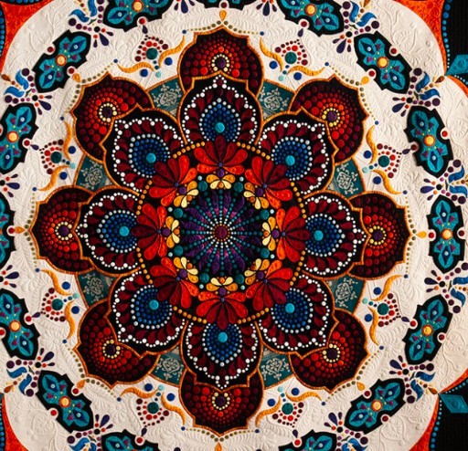 Ornate mandala quilt with beaded floral design in rich red, blue and orange colors on cream fabric