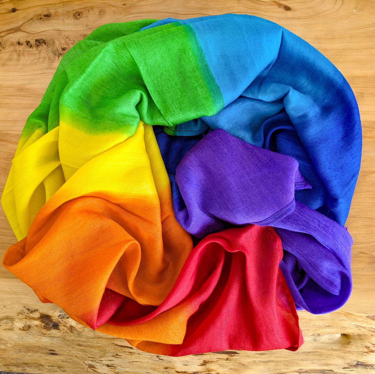 Rainbow-colored silk scarf arranged in flowing folds on wooden table