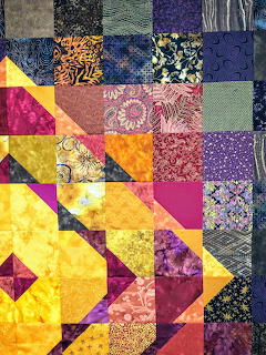 Colorful patchwork quilt with geometric triangle patterns in yellow, purple, pink and blue fabrics