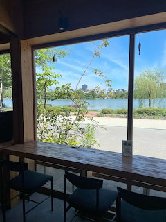 Cafe interior with wooden counter and stools facing a large window with river and city skyline view