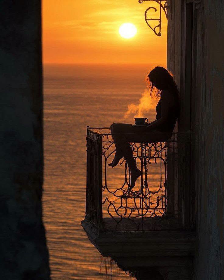 Silhouette of a woman on a balcony above the ocean at sunset