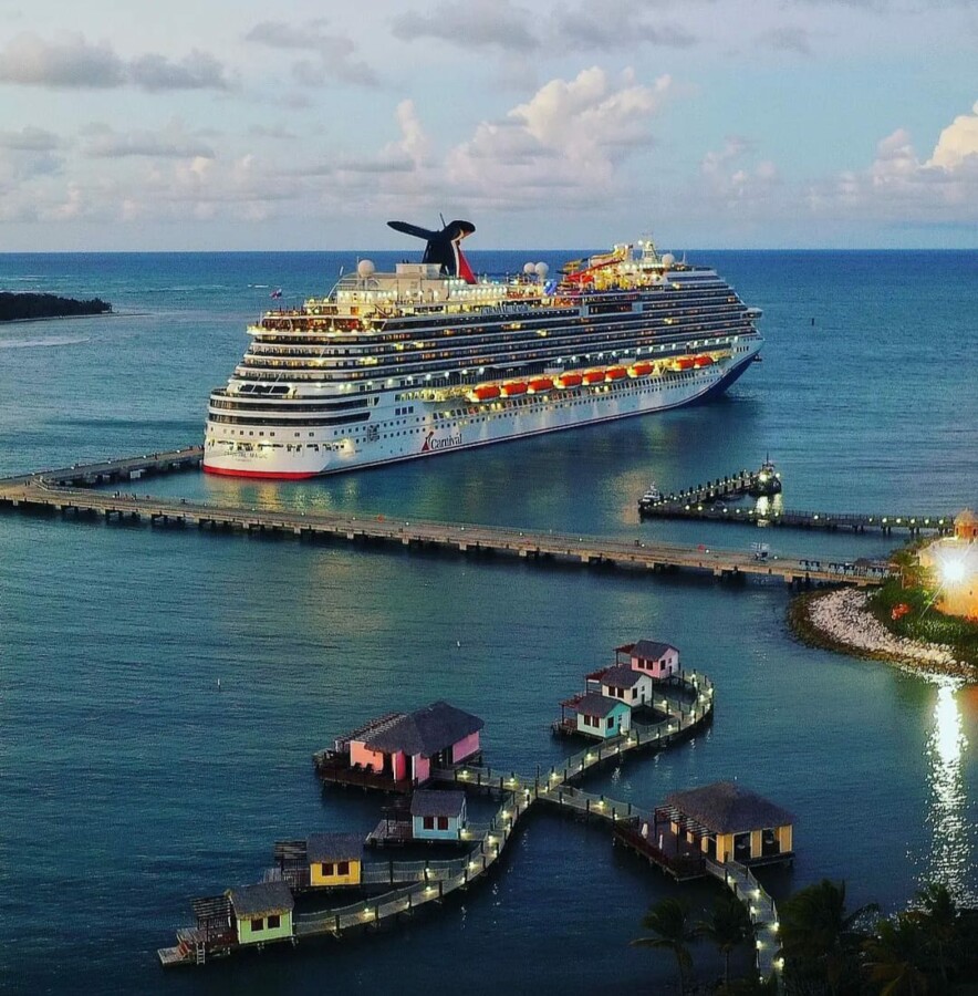 Cruise ship docked in blue water near a pier with small overwater buildings in the foreground