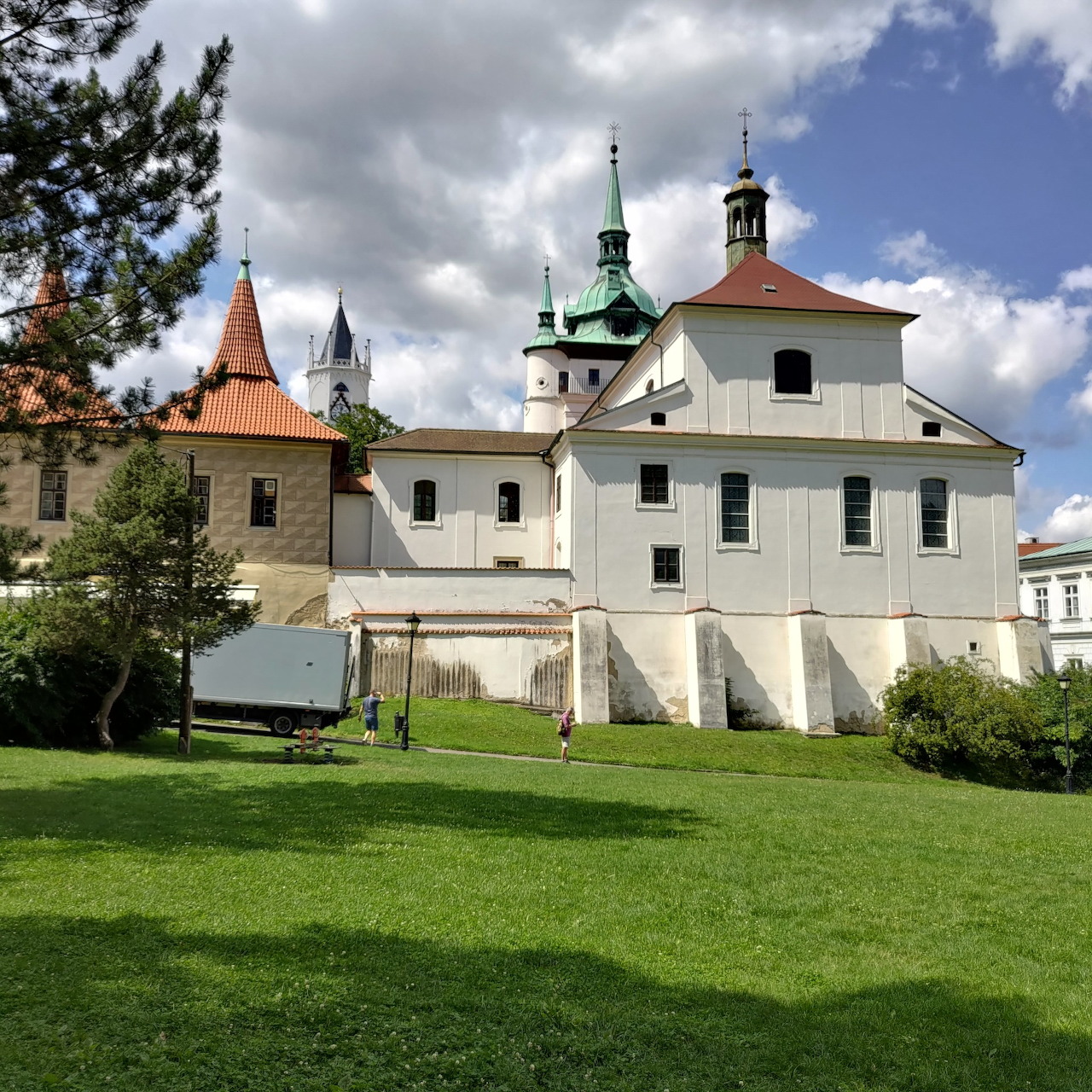 White castle with green-roofed towers and orange turret on green lawn under cloudy sky