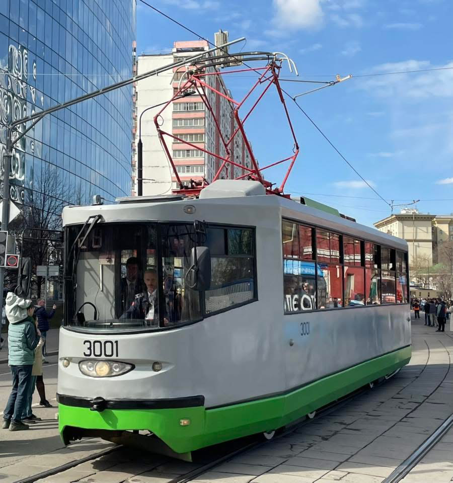 Silver and green tram on city tracks beside modern buildings under a blue sky