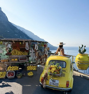 Colorful lemon market stall with yellow vintage car on Amalfi Coast road overlooking the sea