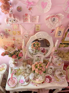 Pink shaby chic vanity table with roses, mirror, teacups, and lace decorations against a pink wall