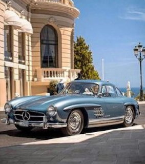 Blue vintage Mercedes-Benz 300SL Gullwing coupe parked in front of a grand Mediterranean building