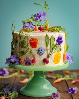 Frosted cake decorated with edible flowers and vegetables on a green cake stand