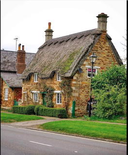 Stone cottage with a thatched roof beside a road and green grass
