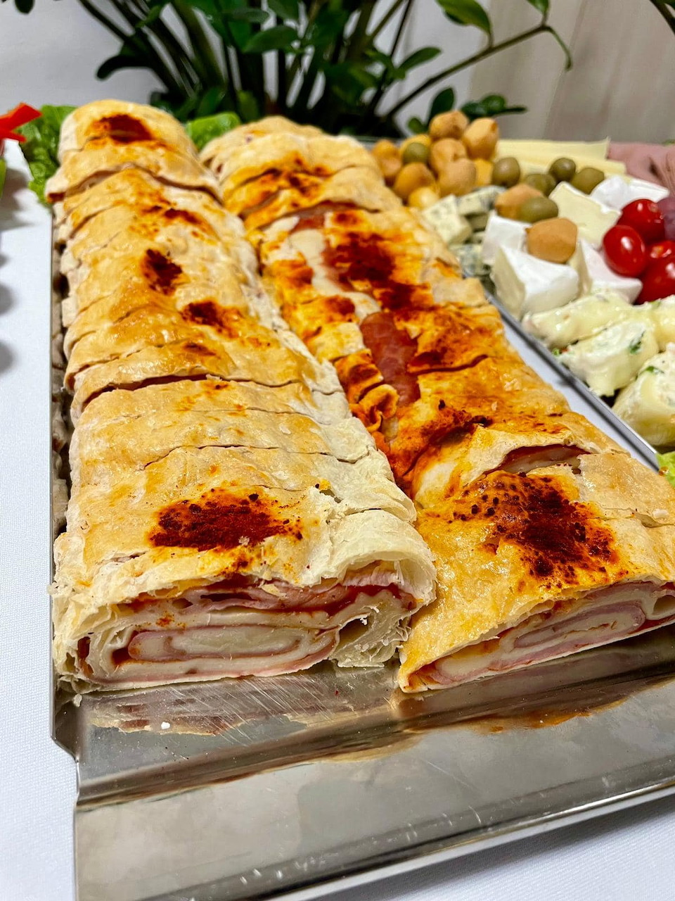 Sliced savory strudel with ham and cheese filling on a silver platter with olives and cheese