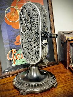 Ornate vintage Bell & Howell movie camera with engraved metal body on decorative pedestal base