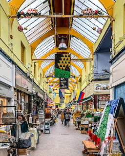 Indoor shopping arcade with yellow roof beams, shops, and people walking through decorated market passage