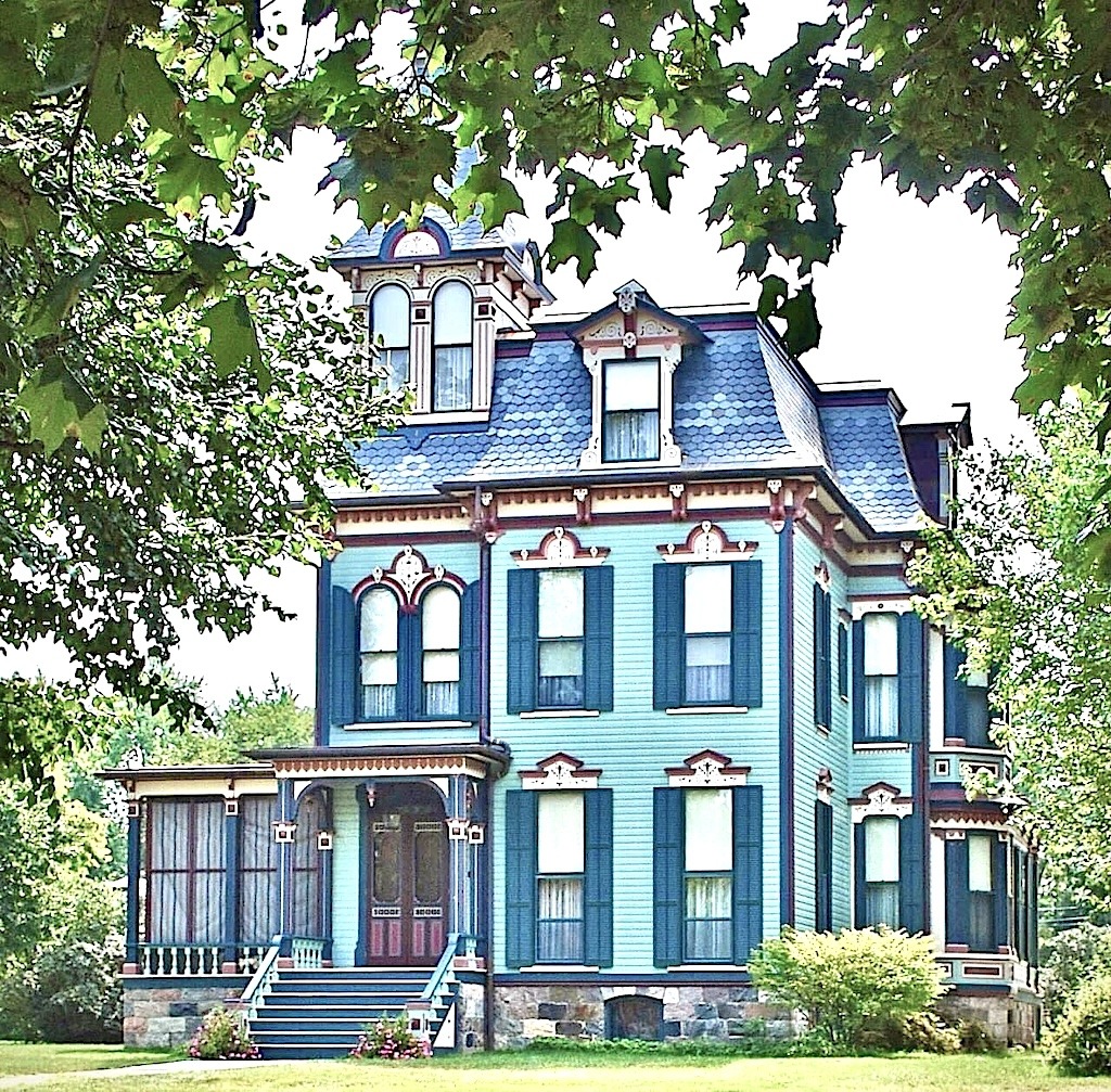Blue Victorian mansion with white trim and ornate architectural details surrounded by green foliage