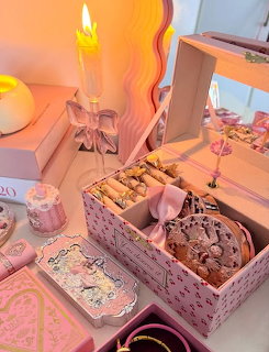 Pink vanity table with open jewelry box, bow decorations, candle, and feminine accessories in warm lighting