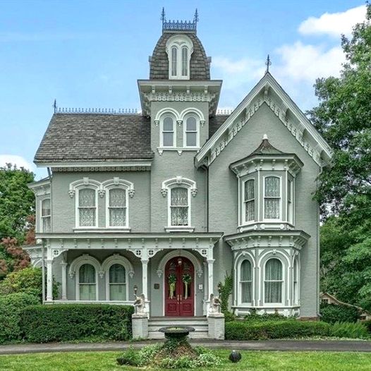 Gray Victorian mansion with white decorative trim, tower, and red door on green lawn