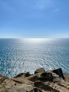 Rocky coastal cliff overlooking sparkling blue Atlantic Ocean with clear sky and sun reflection on water