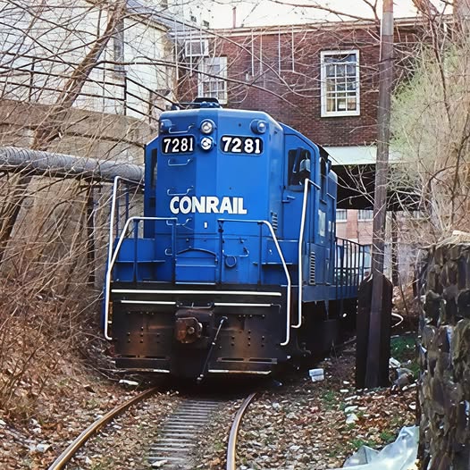 Blue Conrail locomotive 7281 on a curved track near buildings and bare trees
