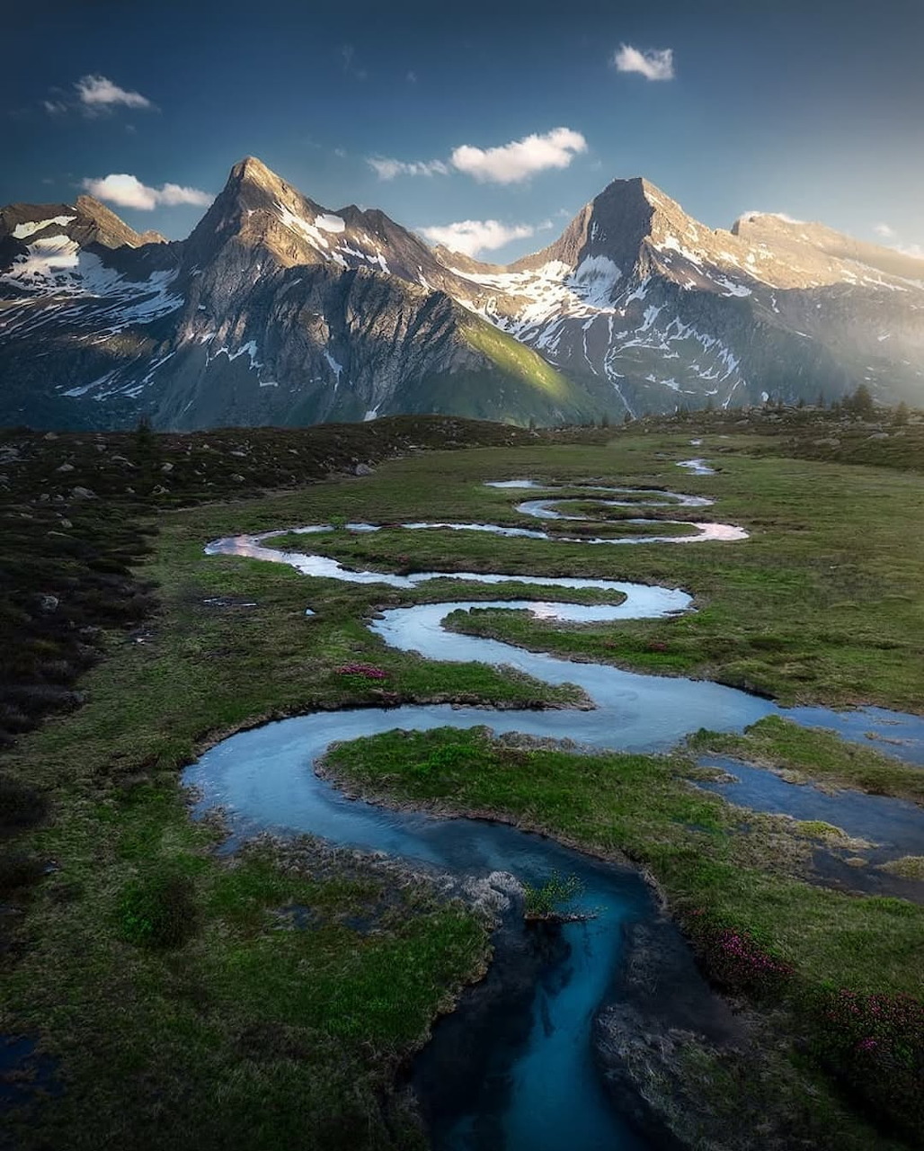 Winding blue river through green alpine valley with snow-capped peaks in the background