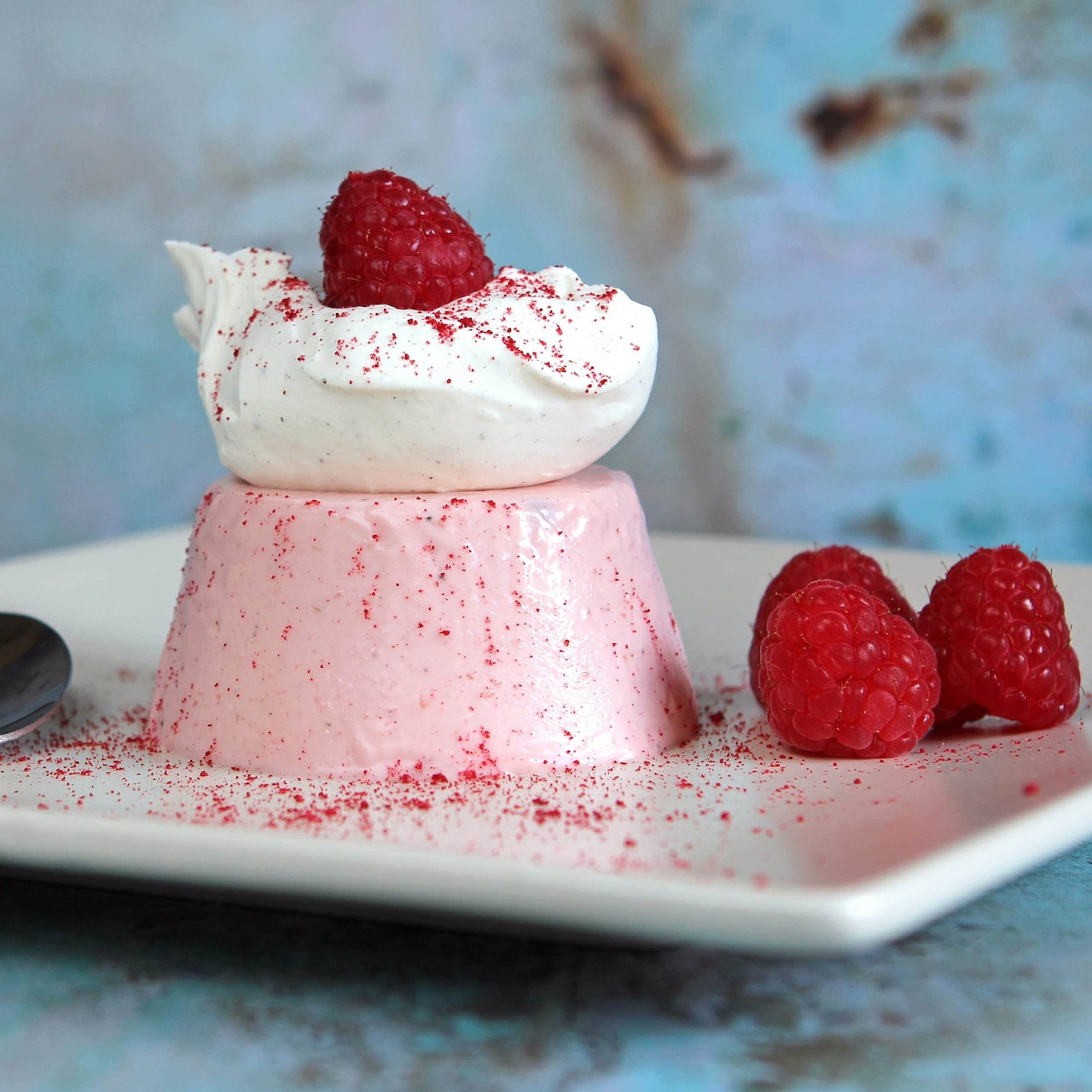 Pink raspberry panna cotta with whipped cream topping and fresh raspberries on white plate