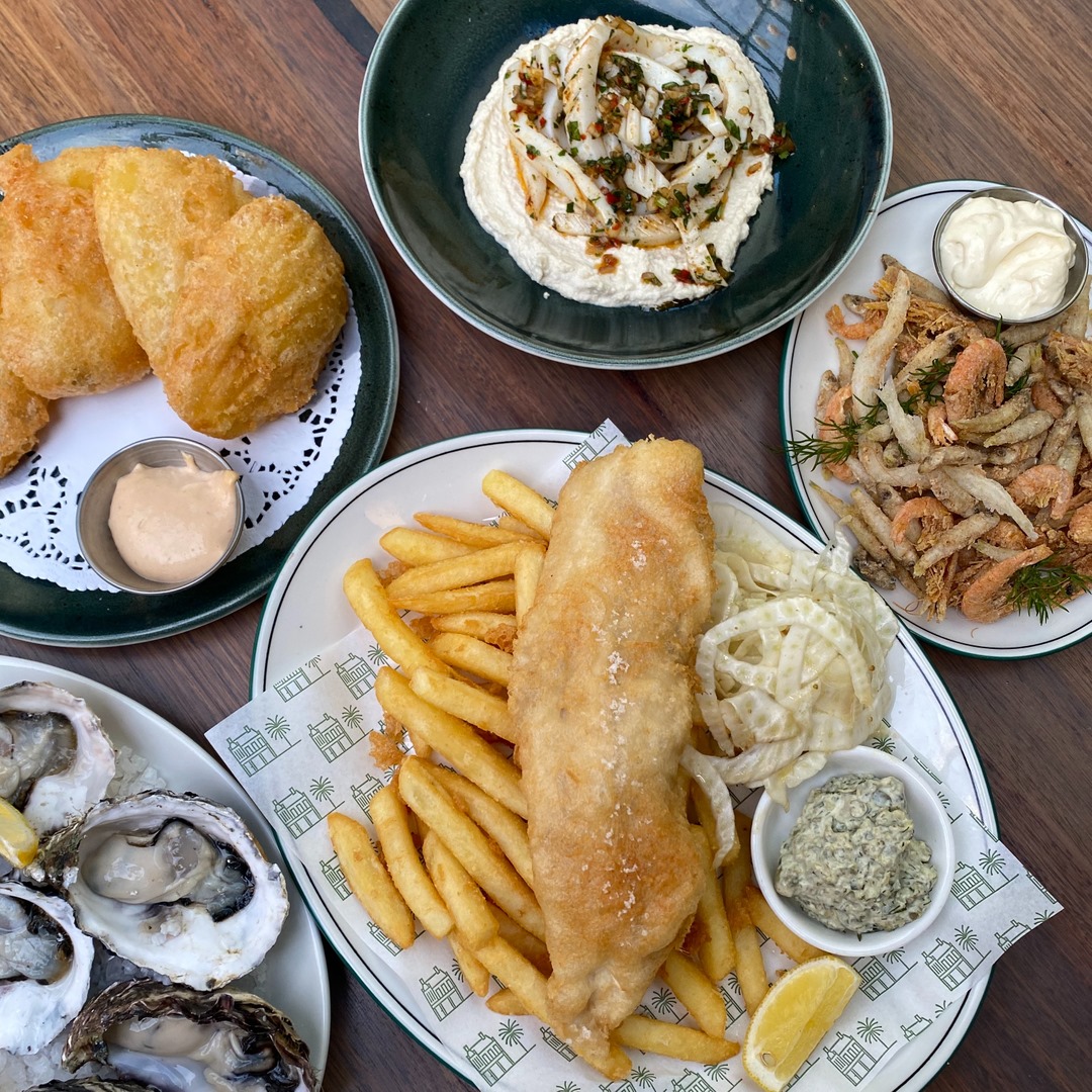 Fish and chips platter with sides, oysters, chicken, and dessert on wooden table
