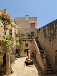 Historic stone courtyard with a fountain, stairs, and plants under a clear blue sky