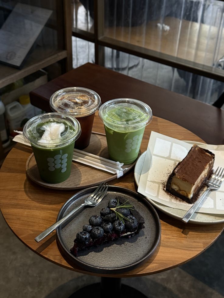 Two iced matcha drinks, a blueberry tart, and a tiramisu cake slice on a café table