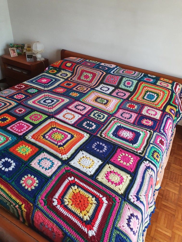 Bed with a colorful crocheted granny square blanket in a simple bedroom